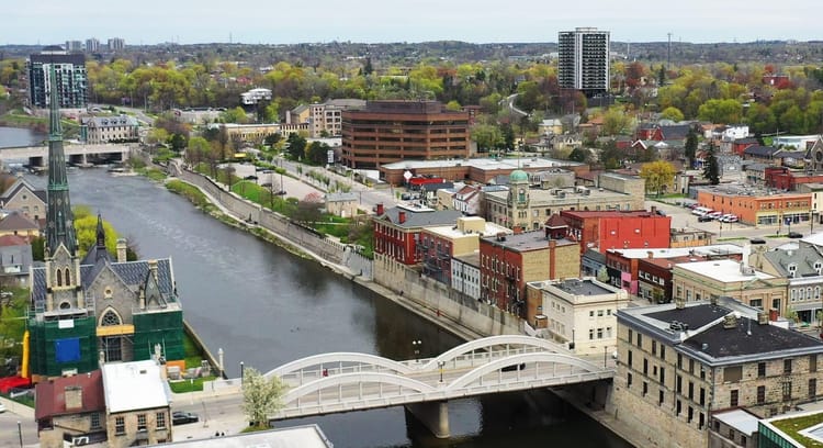 Aerial view of central Galt in Cambridge, showing historic church and bridge, stone and brick buildings, and more suburban areas beyond that.